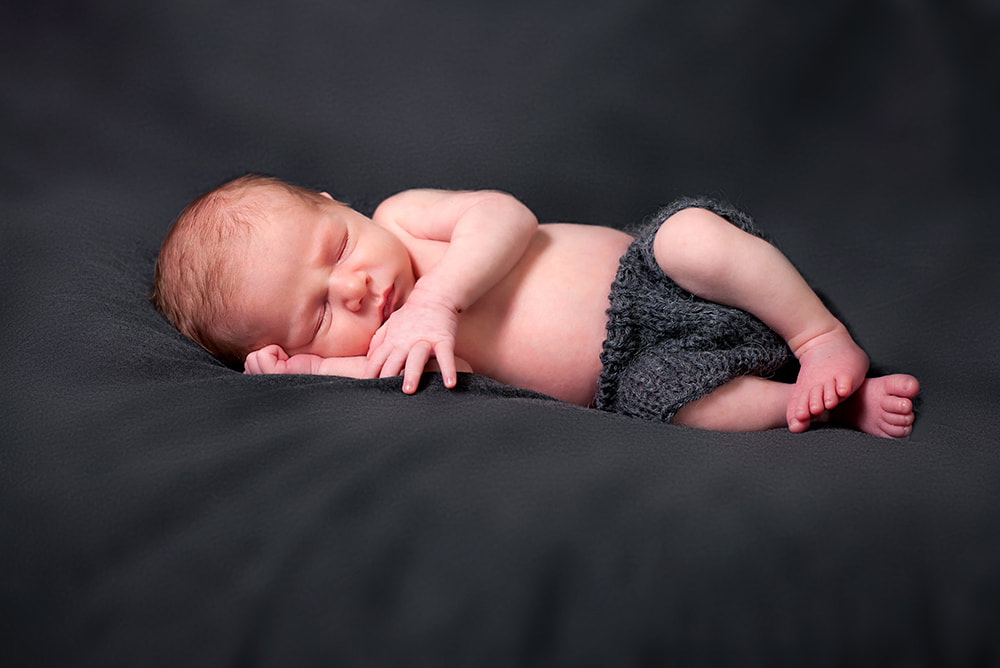 Newborn baby sleeping on his side on dark gray background