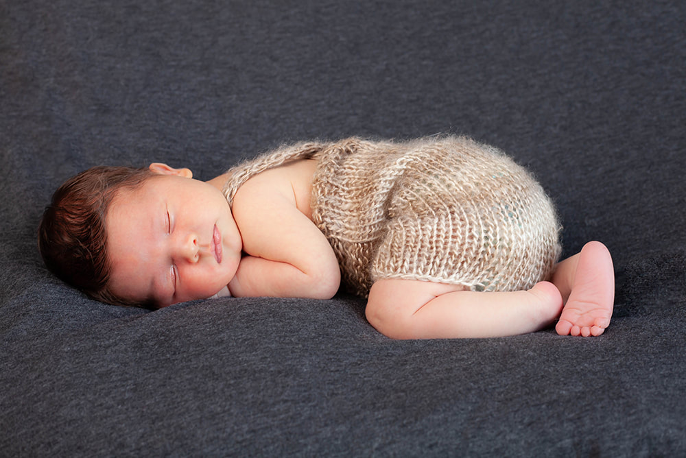 sleeping baby girl in a brown and tan romper on a dark gray background